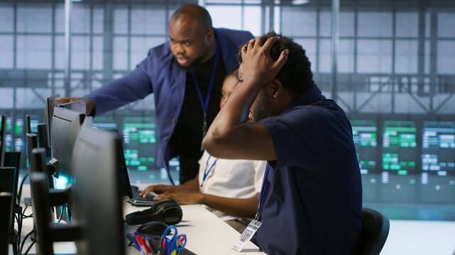 Server room engineers panicking after seeing disaster recovery plans fail, unable to avoid downtime. Stressed data center workers frightened after seeing performance drop while monitoring it, camera A