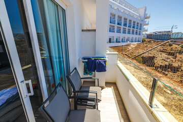 Fototapeta premium Hotel balcony on mountain top in Gran Canaria with stone railing, drying clothes, black chairs and safety net overlooking Atlantic Ocean. 