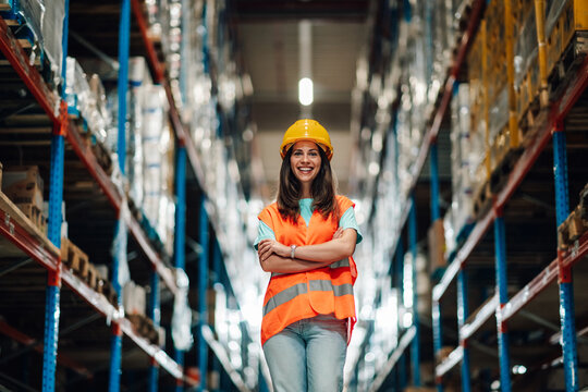 Smiling female supervisor posing with crossed arms in warehouse corridor