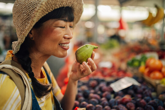 Asian woman savoring pear fragrance at market with fresh produce