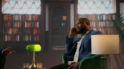 Black gentleman presents a promising business venture over whiskey to his friend in an upper class vintage social club, embodying elite social networking between huge estate heirs. Camera A.