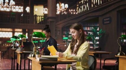 Young teen girl engrossed in reading books at the school library, focusing on literature and knowledge while she is preparing for her academic lessons and other class assignments. Camera A.
