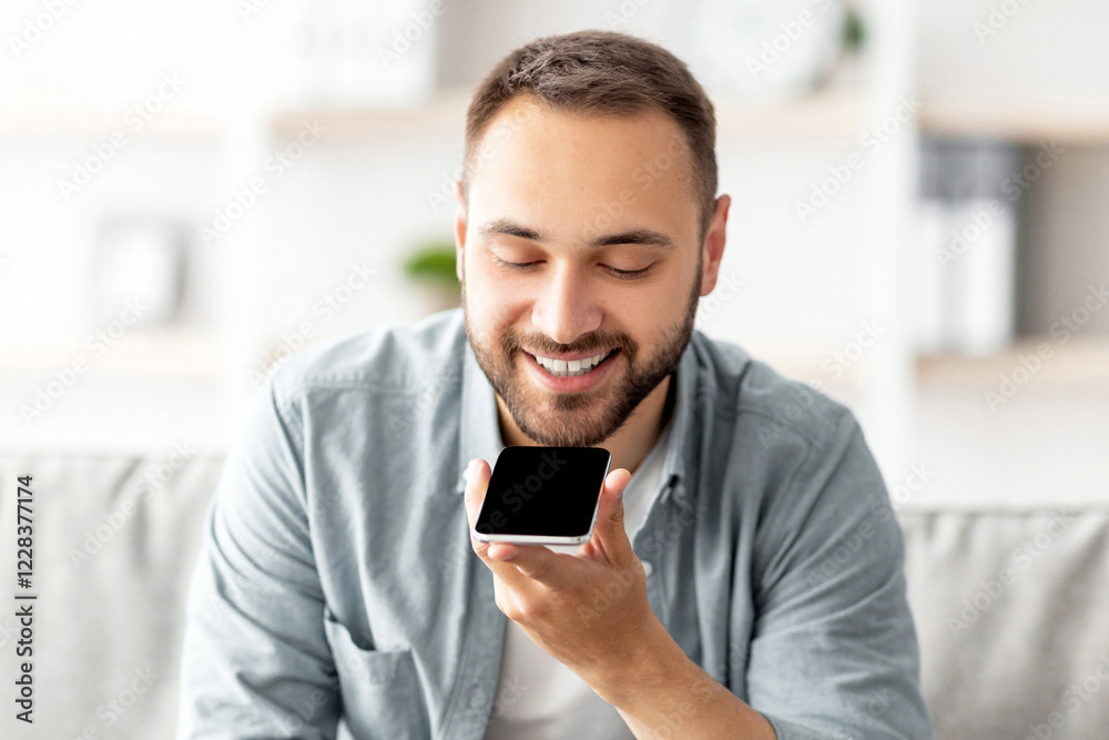 Poster cheerful millennial guy sitting on couch with cellphone at home, mockup for mobile app or website on