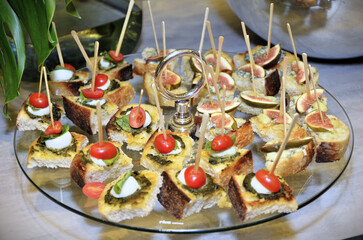 Plate with canapés with pesto sauce, bufula cheese, basil leaves and cherry tomatoes and another canapé with gorgonzola cheese pâté with a slice of fig