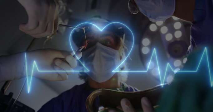 Image of cardiograph with heart over caucasian surgeons with face mask in operating room