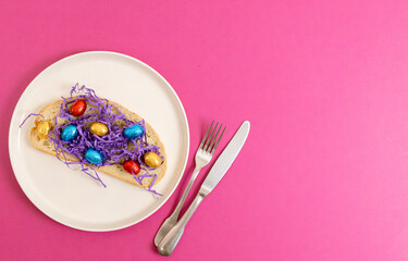 Sandwich with hay and Easter eggs in a plate on a pink background.