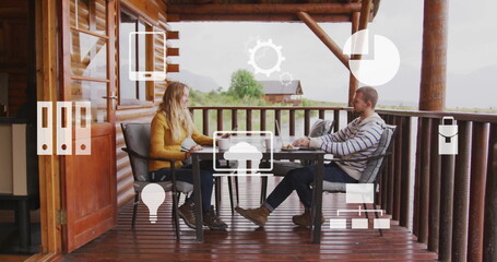 Image of icons and data processing over biracial couple at table on terrace