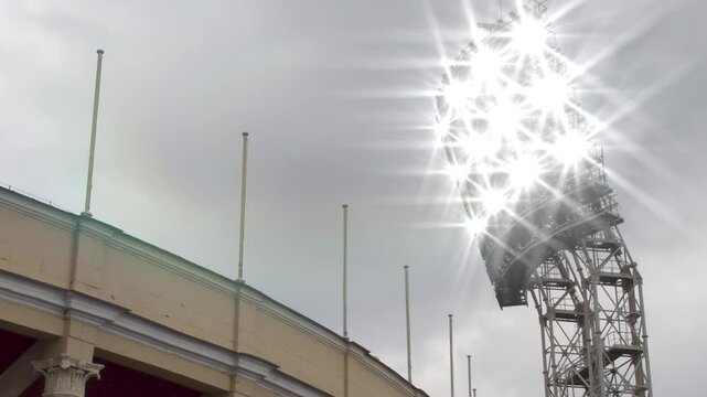 Switching on Stadium Lighting. Loop. Above the open stadium, a large floodlight tower turns on and then off. There are empty flagpoles to place flags
