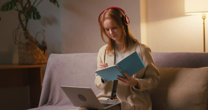 Woman student in headphones looks at laptop making notes
