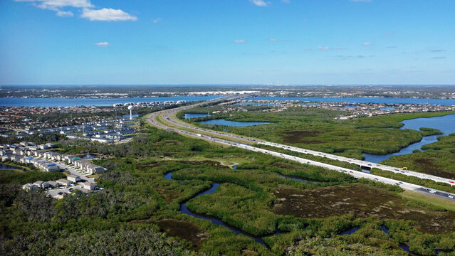 Aerial (drone) view of I-75 looking north across the Manatee River in Bradenton, FL. Beautiful Florida river with lush greenery, houses, a clear blue sky above, and St. Petersburg in the distance.