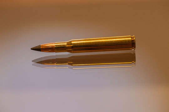 Single 30-06 cartridge lies horizontally on a glass surface, creating a sharp and distinct reflection.