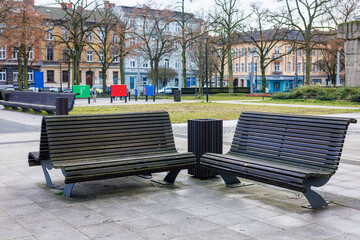 Double and regular wooden benches in a city park. Benches against the backdrop of trees and houses. A place to relax in the city.