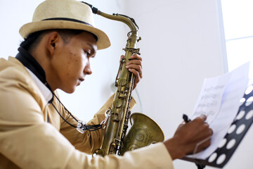 Side View Of Young Male Musician With Saxophone Writing On Music Sheet 