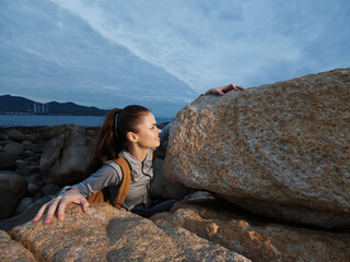 A young woman in athletic clothing climbing rocky terrain by the sea, showcasing determination and...