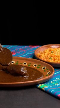 Vertical video, serving mole poblano sauce on a clay plate with a piece of chicken, food from mexico
