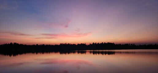 Stunning sunset over tranquil lake, reflecting warm hues of orange,pink,blue. Peaceful water and soft sky create serene and dreamy atmosphere, perfect for backgrounds, nature prints, landscape themes.