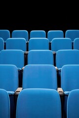 Fototapeta premium Rows of empty blue chairs in a theater setting against black background.