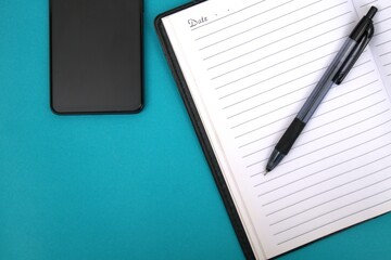 An open notebook with a ballpoint pen on it and a smartphone next to it on a blue table