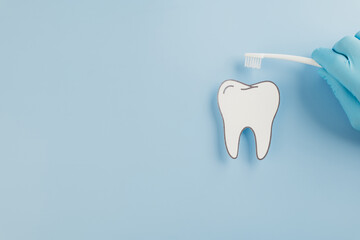 A gloved doctor holds a toothbrush with a paper tooth for Dentist Day