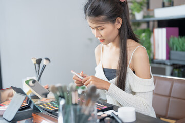 Asian woman applying make up foundation and concealer make up on face with cosmetics makeover Daily beauty routine at home.