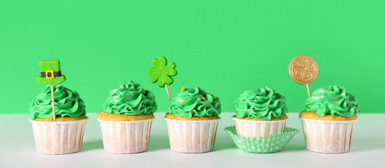 Tasty cupcakes for St. Patrick's Day on white table against green background