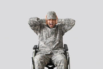 Young soldier in wheelchair screaming on light background