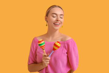 Pretty young woman with maracas on orange background