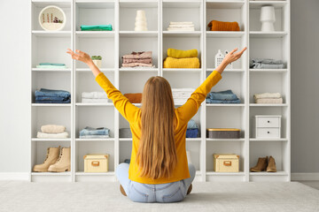 Young woman sitting on floor near shelves with different clothes at home