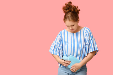 Beautiful young woman with hot water bottle suffering from menstrual cramps on pink background