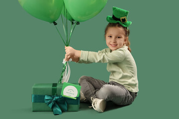 Cute little girl with leprechaun's hat, gift box and balloons on green background. St. Patrick's...