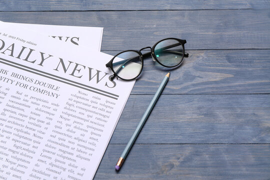 Newspapers with glasses and pencil on blue wooden background