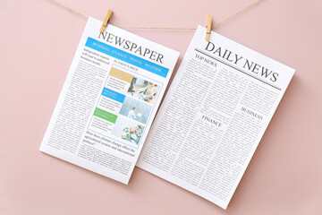 Different newspapers hanging on rope against pink background