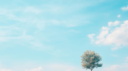 Obraz premium Solitude in the Azure: A lone tree stands silhouetted against a vast expanse of azure sky, adorned with wispy white clouds, evoking a sense of tranquility and contemplation.