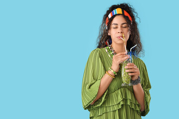 Beautiful young happy African-American woman with glass of tasty kiwi smoothie on blue background