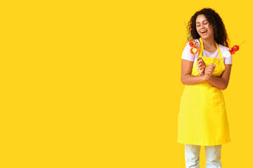 Beautiful young happy African-American woman with tasty grilled vegetables skewers on yellow...