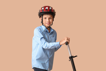 Cute schoolboy in helmet with modern electric kick scooter on brown background