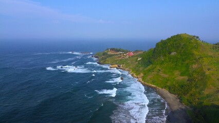 Fototapeta premium Aerial drone view of coastline with hills and trees, as well as view of coral cliffs and sea with waves from the ocean in Pecaron Beach Kebumen Central Java Indonesia