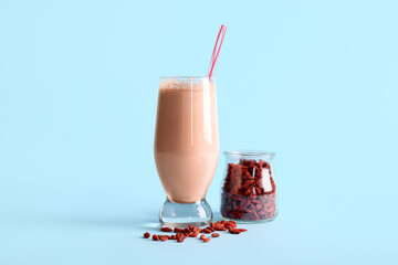 Glass of fresh goji smoothie and jar with berries on blue background