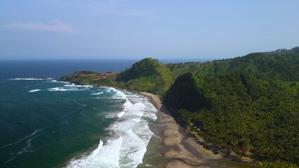 Aerial drone view of coastline with hills and trees, as well as view of coral cliffs and sea with waves from the ocean in Pecaron Beach Kebumen Central Java Indonesia