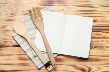 Blank recipe book, spoon, fork and napkin on wooden background