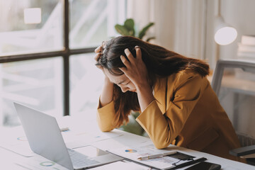 Young Asian businesswoman working on laptop computer, stressed has a headache and thinks hard from...