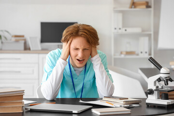 Stressed male medical intern studying at table in clinic