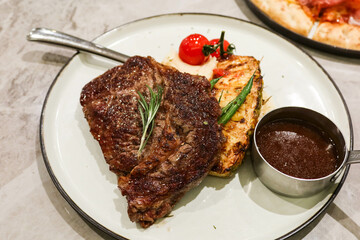 close up of grilled beef steak with pineapple and cherry tomato on the side and barbecue sauce gravy on a white plate