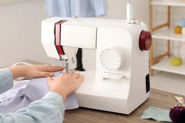 Young female tailor using sewing machine near table in atelier, closeup