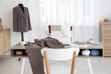 Tailor's workplace with sewing machine, different supplies and mannequin in atelier