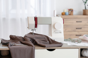Modern sewing machine with brown fabric and tailor's supplies on table in atelier