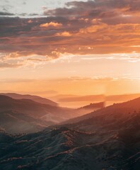 Obraz premium Sunset over a mountainous landscape with layers of hills and valleys, the sky filled with warm orange