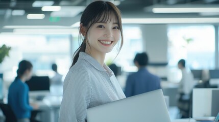 Fototapeta premium Smiling Japanese businesswoman standing in an office, holding her laptop. She is wearing casual clothes, and other people working behind her are blurred.,generated ai.
