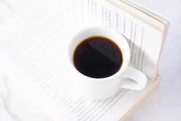 ページを開いたペーパーバック（洋書）とコーヒーの入ったコーヒーカップで、コーヒーを飲みながら読書を楽しんでいるイメージ
