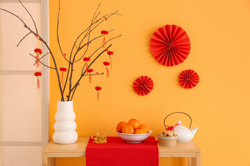 Vase with tree branches, Chinese food and teapot for New Year celebration on shelf near yellow wall in room